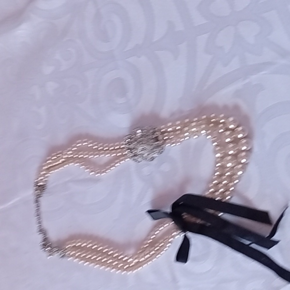 Three strand graduated pearl necklace with a crystal brooch and black ribbon .